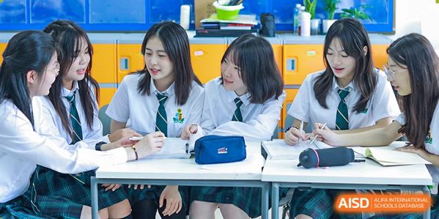 Two female students at Shanghai International High School of BANZ smiling and talking to each other at a desk in their classroom.