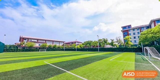 A landscape image of a well-maintained sports field at Shanghai International High School of BANZ with a building in the background.