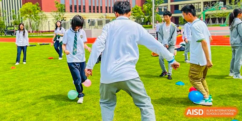 Students from Shanghai International High School of BANZ playing a game with balloons on a grassy field.