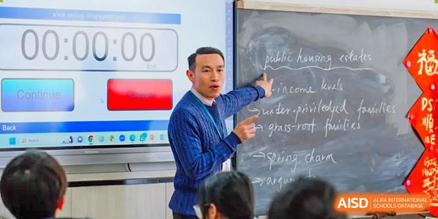 A teacher at The Affiliated School of JNU for Hong Kong & Macau Students (ASJ Dongguan) is teaching a class at the blackboard.