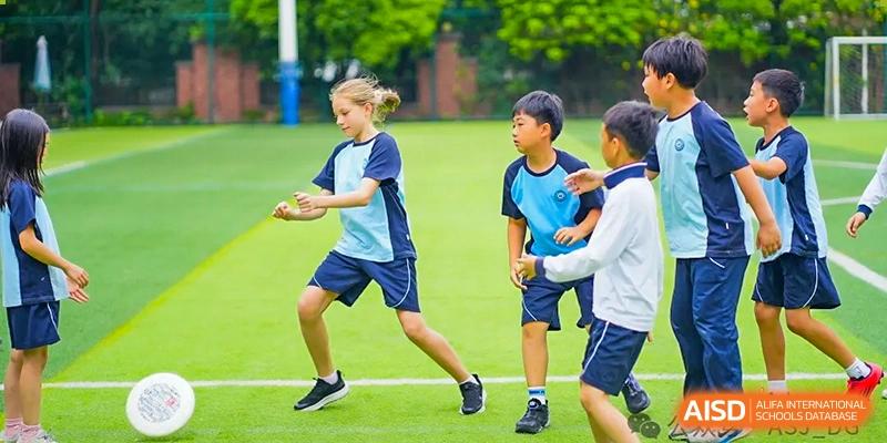 Two students from The Affiliated School of JNU for Hong Kong & Macau Students (ASJ Dongguan) are playing a game on a grass field.
