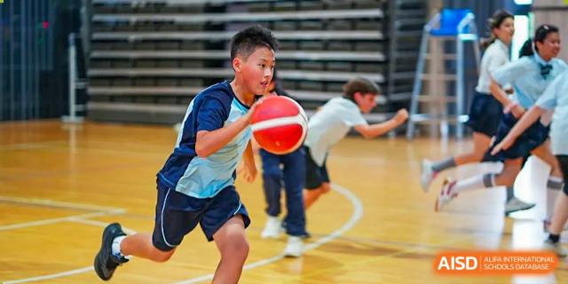 A student from The Affiliated School of JNU for Hong Kong & Macau Students (ASJ Dongguan) is dribbling a basketball during a game.
