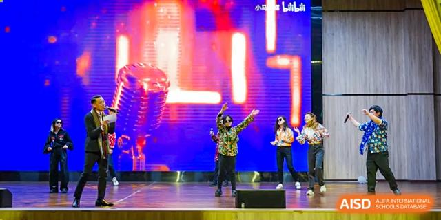 Students from The Affiliated School of JNU for Hong Kong & Macau Students (ASJ Dongguan) are performing on a stage.
