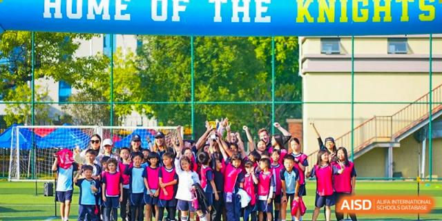 A large group of students from The Affiliated School of JNU for Hong Kong & Macau Students (ASJ Dongguan) are cheering at a sports event.