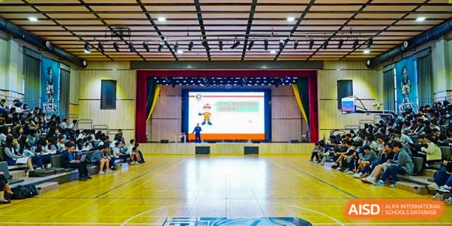 A stage with a screen and a scoreboard in a gymnasium at The Affiliated School of JNU for Hong Kong & Macau Students (ASJ Dongguan).