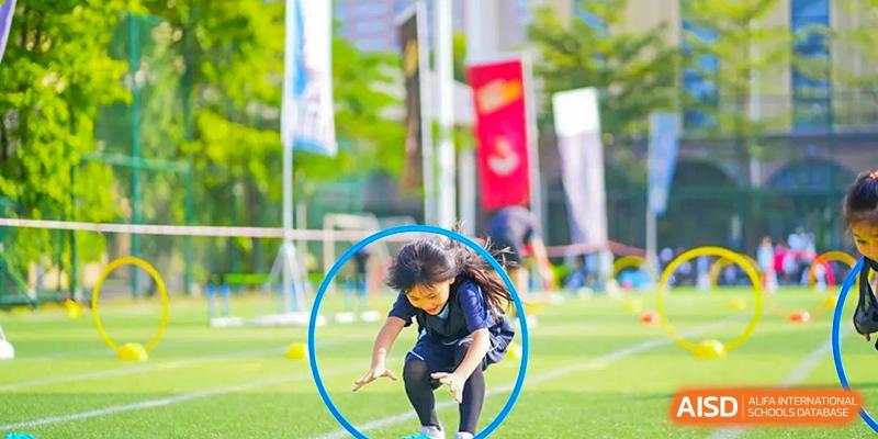 A student from The Affiliated School of JNU for Hong Kong & Macau Students (ASJ Dongguan) is participating in an outdoor sport by jumping through a blue hoop.