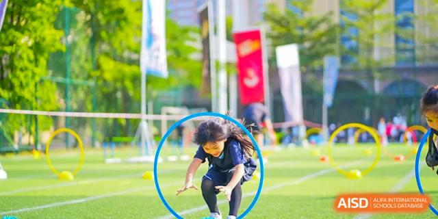 A student from The Affiliated School of JNU for Hong Kong & Macau Students (ASJ Dongguan) is participating in an outdoor sport by jumping through a blue hoop.
