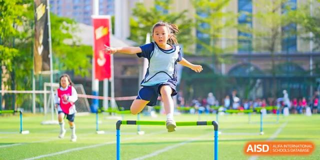 A student from The Affiliated School of JNU for Hong Kong & Macau Students (ASJ Dongguan) is jumping over a hurdle on a grass field.