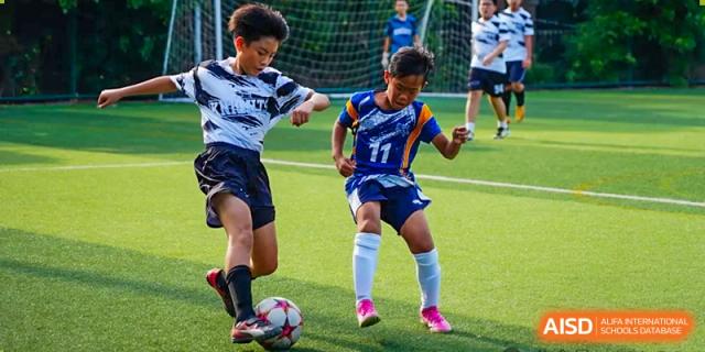 Two students from The Affiliated School of JNU for Hong Kong & Macau Students (ASJ Dongguan) are playing soccer on a grass field.