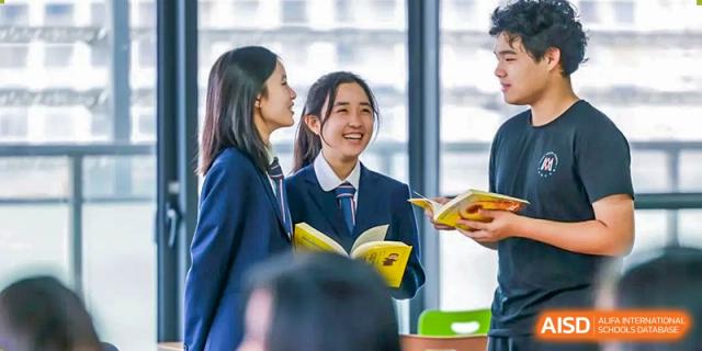Two female students in school uniforms are looking at a book and smiling at Vanke Meisha Academy.