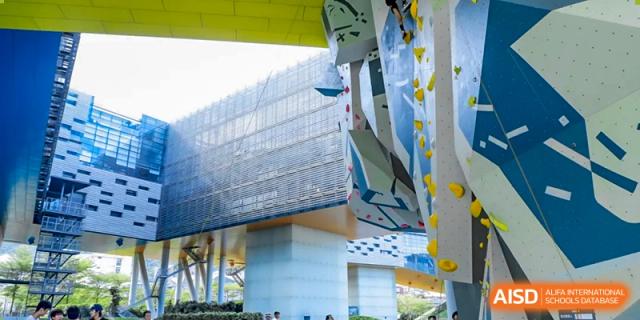 A tall, modern rock climbing wall is attached to the side of a building at Vanke Meisha Academy.