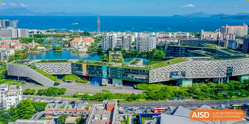 An aerial view of a large, modern building with a green rooftop and nearby city and ocean views at Vanke Meisha Academy.