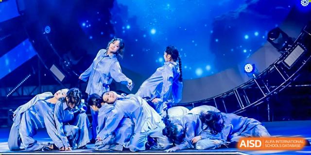 Female students are performing a dance routine on a stage with bright blue lights at Vanke Meisha Academy.