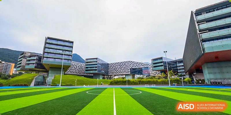 A large, modern building overlooks a bright green soccer field at Vanke Meisha Academy.