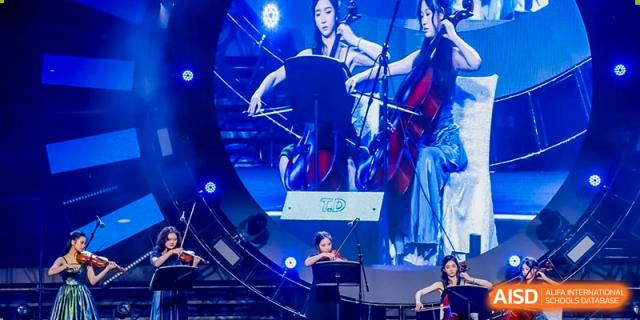 Female students play the cello on a dark stage with vibrant blue lighting at Vanke Meisha Academy.