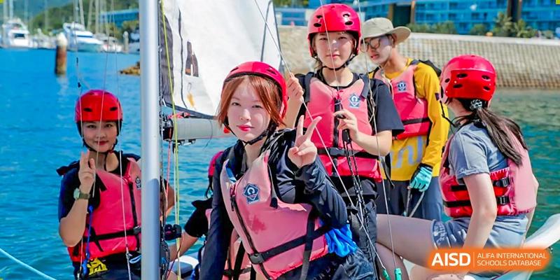 Two female students wearing life vests and helmets smile while on a sailboat at Vanke Meisha Academy.
