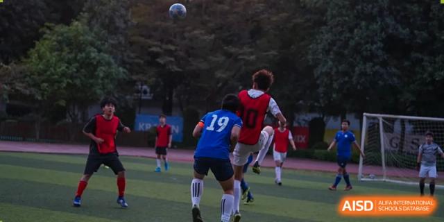 Two male students wearing red and blue uniforms are playing soccer at Vanke Meisha Academy.