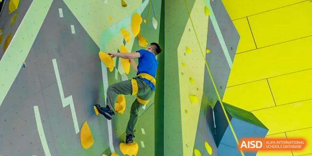 A male student is rock climbing while wearing a yellow shirt and safety harness at Vanke Meisha Academy.