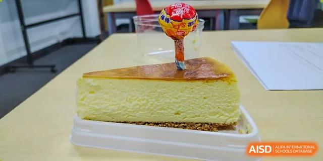 A slice of cheesecake with a lollipop on top is on a white plate at Vanke Meisha Academy.