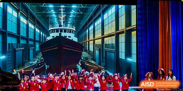 A group of students in red t-shirts with a ship in the background at Yew Chung International School of Chongqing