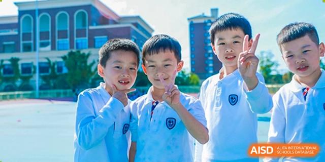 Two young male students from Yiwu International Academy smiling and posing outdoors in their school uniform.