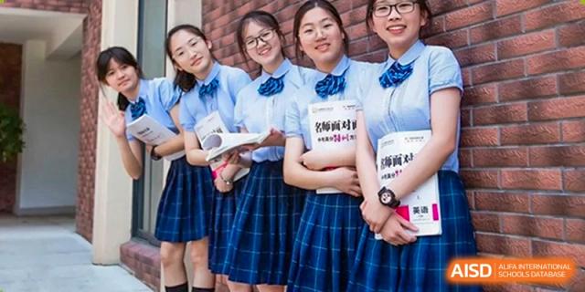 A group of female students from Yiwu International Academy in plaid skirts and white shirts holding books and smiling.