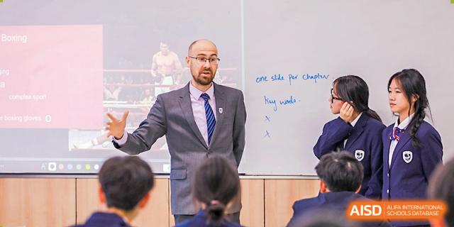 A male teacher in a suit and tie lecturing to students in a classroom at Yiwu International Academy.