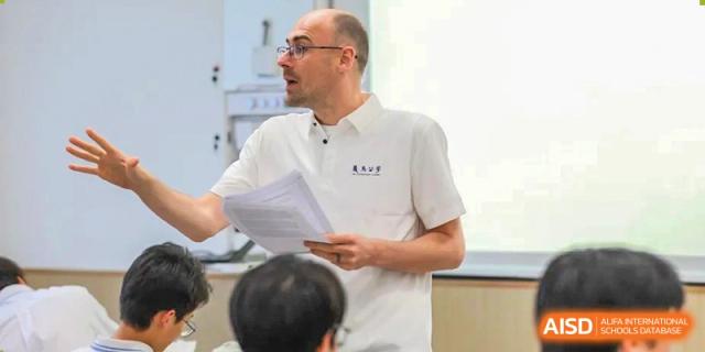 A male teacher in a white polo shirt addressing students in a classroom at Yiwu International Academy.
