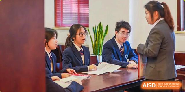 Students in blazers and ties engaging in a discussion around a table in a classroom at Yiwu International Academy.