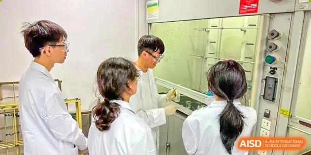 Students in lab coats working in a science laboratory, likely under a fume hood, at Yiwu International Academy.