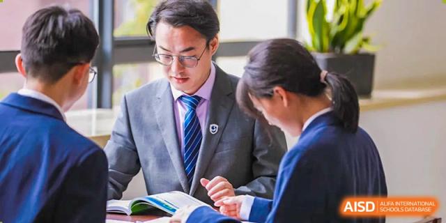 A male student in a suit and tie working closely with a female student on a document at Yiwu International Academy.