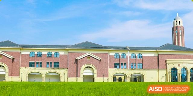 The exterior of a school building with red brick and a pitched roof, fronted by green grass, at Yiwu International Academy.