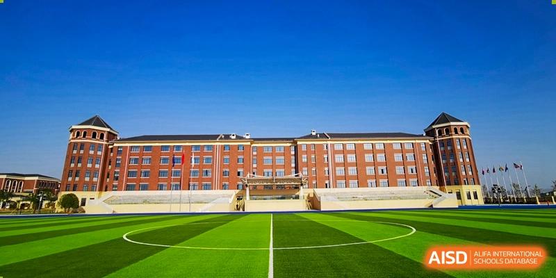 The main academic building and a striped green sports field under a clear blue sky at Yiwu International Academy.