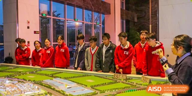 Students from Yiwu International Academy observing and discussing a detailed scale model of a building or city plan.