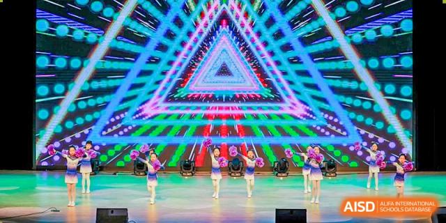 Students performing a choreographed dance routine on a brightly lit stage with a geometric background at Yiwu International Academy.