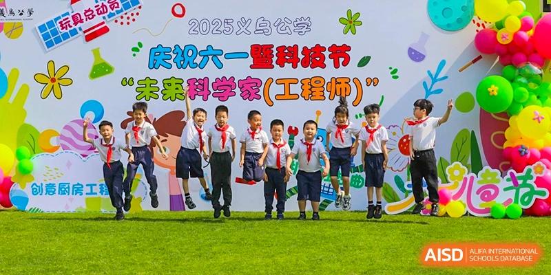 A group of young students from Yiwu International Academy in uniforms posing outdoors beneath a banner related to science and technology.