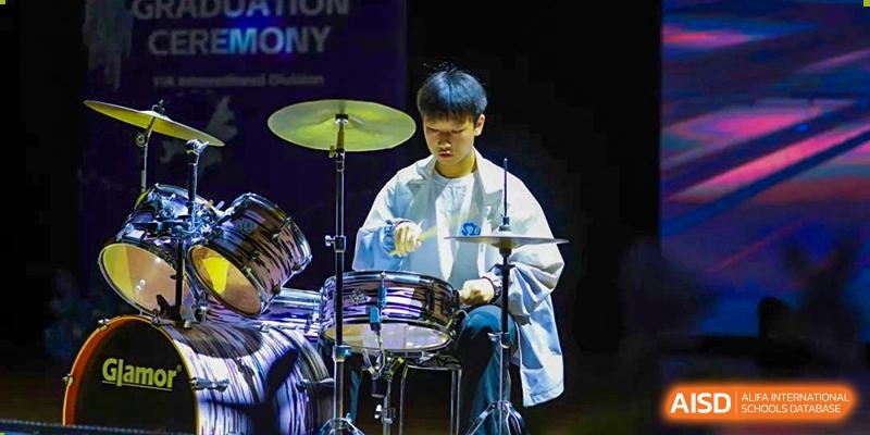 A student from Yiwu International Academy playing the drums intensely during a musical performance.