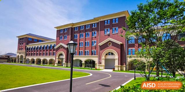 The exterior of a red brick school building with a curved driveway and lamp post at Yiwu International Academy.