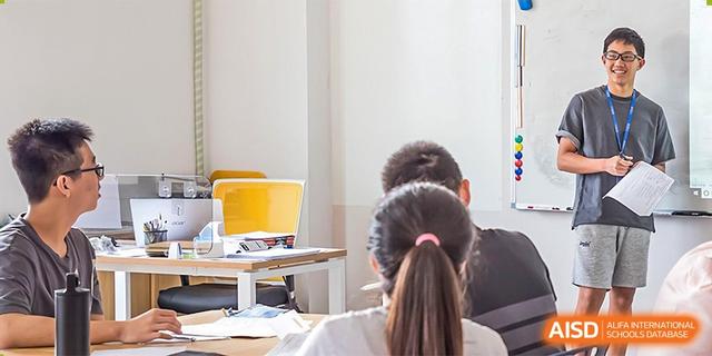 A view from behind students of a person's back and long hair, attentively looking toward the front of the classroom at BASIS International School Hangzhou (BIHZ).