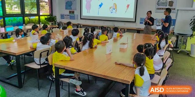 A classroom of young students sitting around a large wooden table, watching a presentation on a projected screen at BASIS International School Hangzhou (BIHZ).