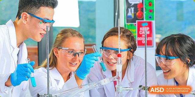 A teacher wearing safety goggles and a lab coat working with a student on a science experiment involving glassware and liquid at BASIS International School Hangzhou (BIHZ).