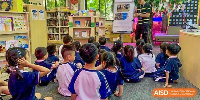 A group of young students in school uniforms sitting on the floor and looking toward a teacher or presentation in a classroom at BASIS International School Hangzhou (BIHZ).