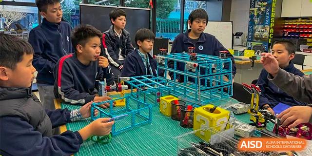 Three male students working on a complex robotics or building project made of blue and black parts on a table at BASIS International School Hangzhou (BIHZ).