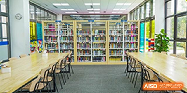 A wide shot of a section of the school library with tall shelves full of books and a row of tables and chairs at BASIS International School Hangzhou (BIHZ).