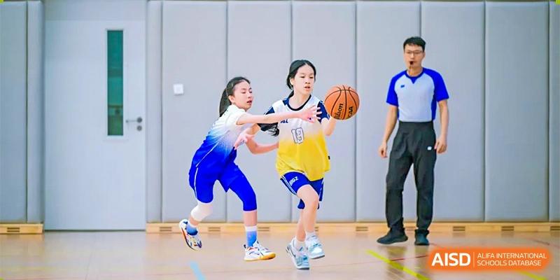 Two female students playing basketball, with one in a yellow jersey dribbling the ball and another defending, at BASIS International School Hangzhou (BIHZ).