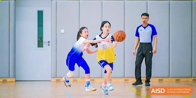 Two female students playing basketball, with one in a yellow jersey dribbling the ball and another defending, at BASIS International School Hangzhou (BIHZ).