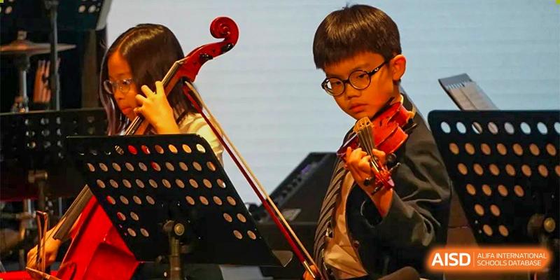 A young male student focused on playing the violin during a musical performance on a stage at BASIS International School Hangzhou (BIHZ).