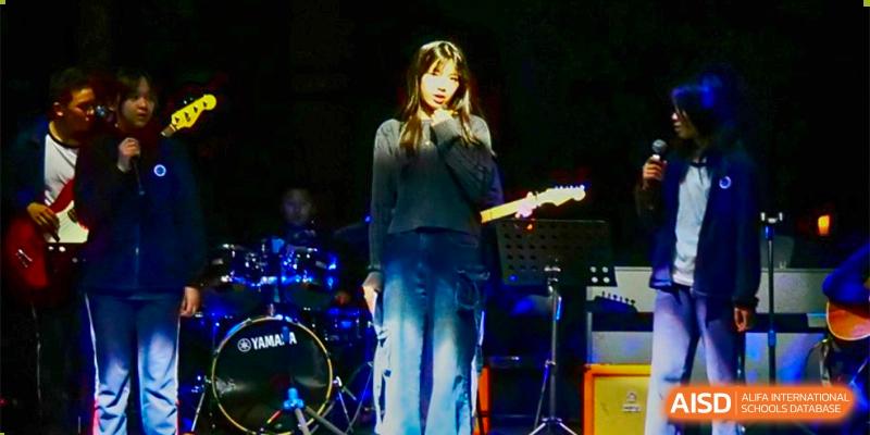 A female student singing on stage while holding a microphone, with a guitar visible in the background at BASIS International School Hangzhou (BIHZ).