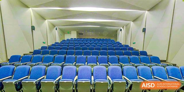 A wide interior shot of a modern, empty auditorium or lecture hall with rows of blue chairs at BASIS International School Hangzhou (BIHZ).