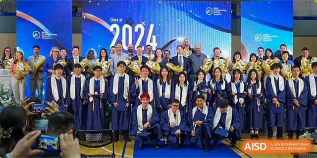 A large group of students in graduation robes and caps posing with faculty and staff on a stage for a ceremony at BASIS International School Hangzhou (BIHZ).
